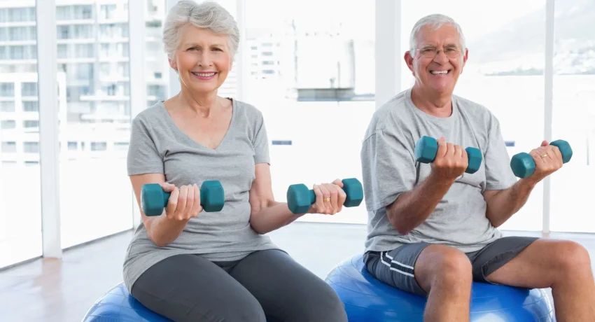 happy-senior-couple-sitting-fitness-balls-with-dumbbells