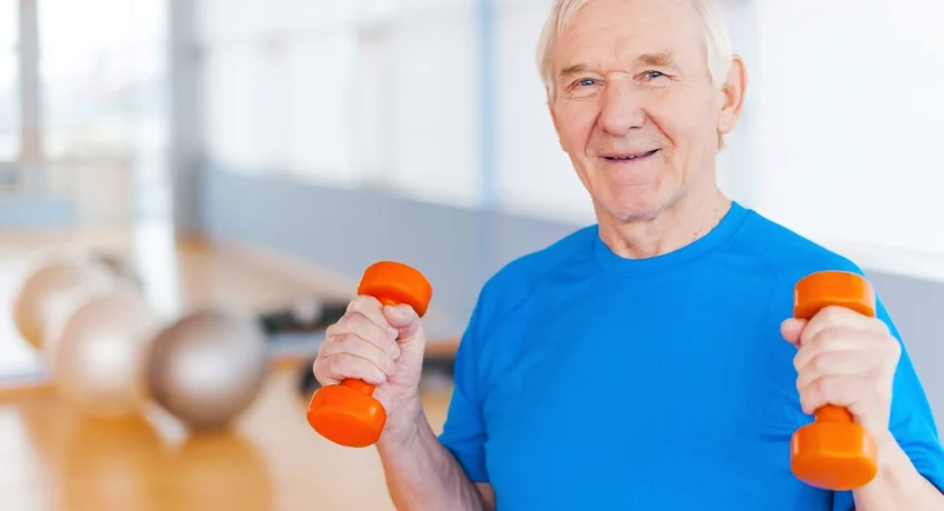 road-recovery-happy-senior-man-exercising-with-dumbbells-smiling-while-standing-indoors