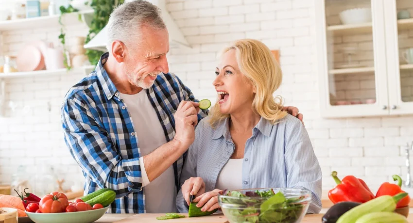 senior-man-feeding-cucumber-slice-her-wife-kitchen